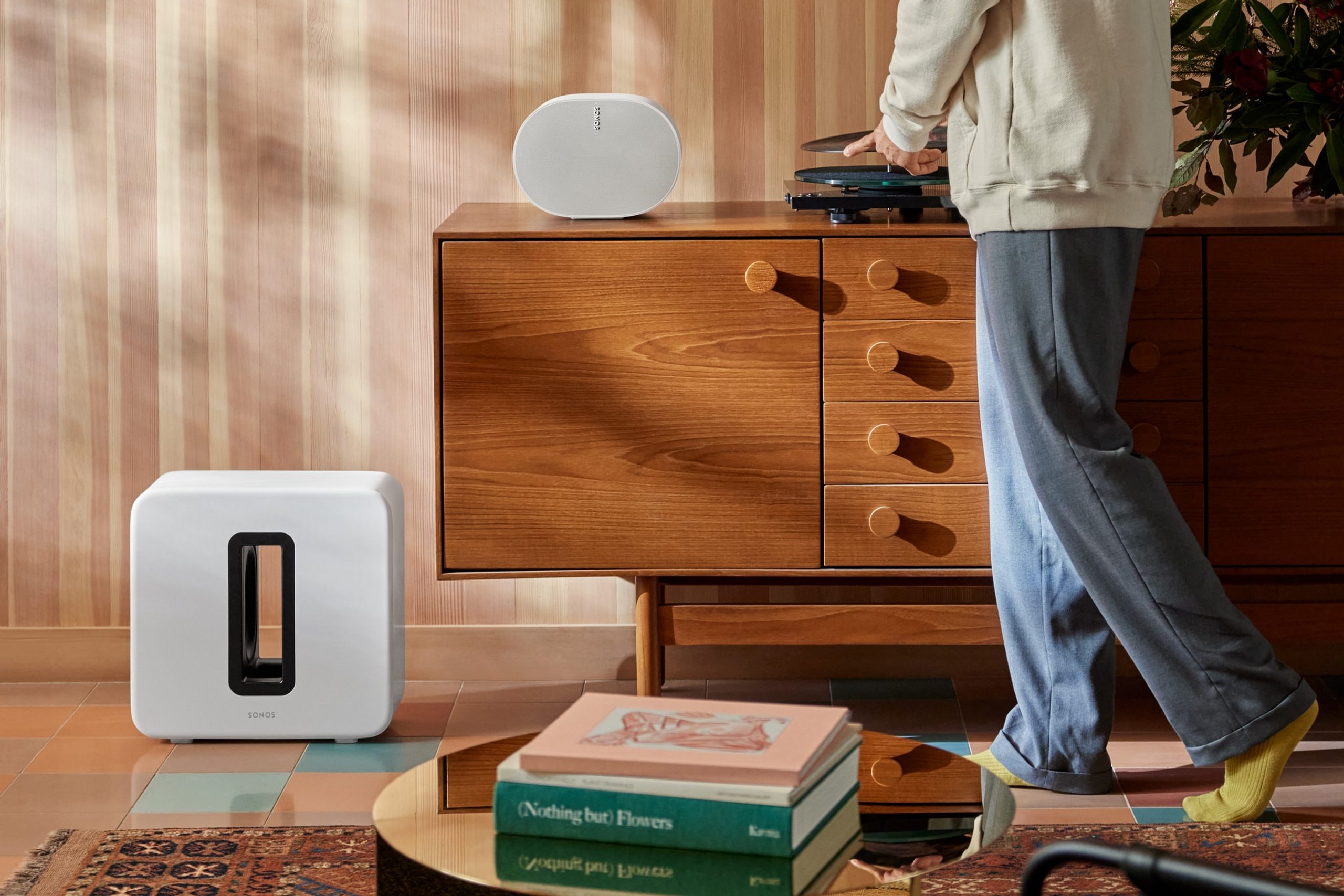 A white Sonos Sub 4 on the floor next to a credenza while a person puts on a vinyl record
